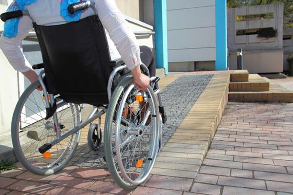 According to the social model of disability, a student using a wheelchair is not disabled by their own physiology, but rather by an inaccessible built environment that lacks necessary accommodations like ramps.