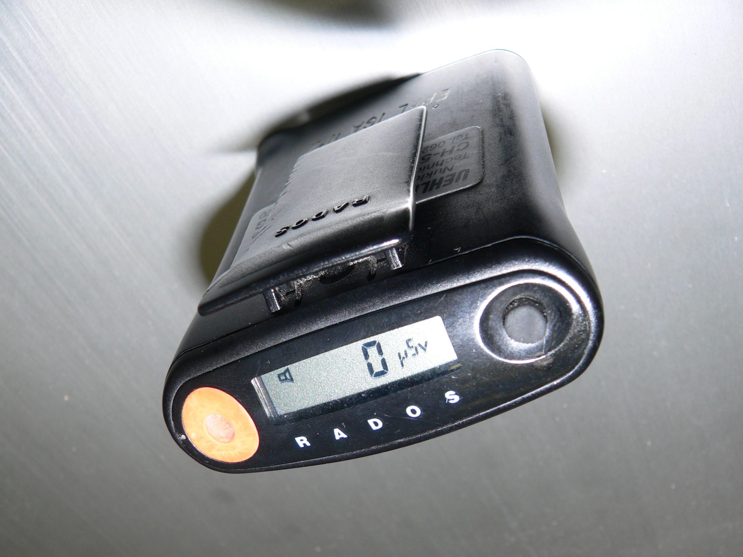 An electronic personal dosimeter clipped to clothing, used by healthcare workers to monitor cumulative radiation exposure over the course of a shift.