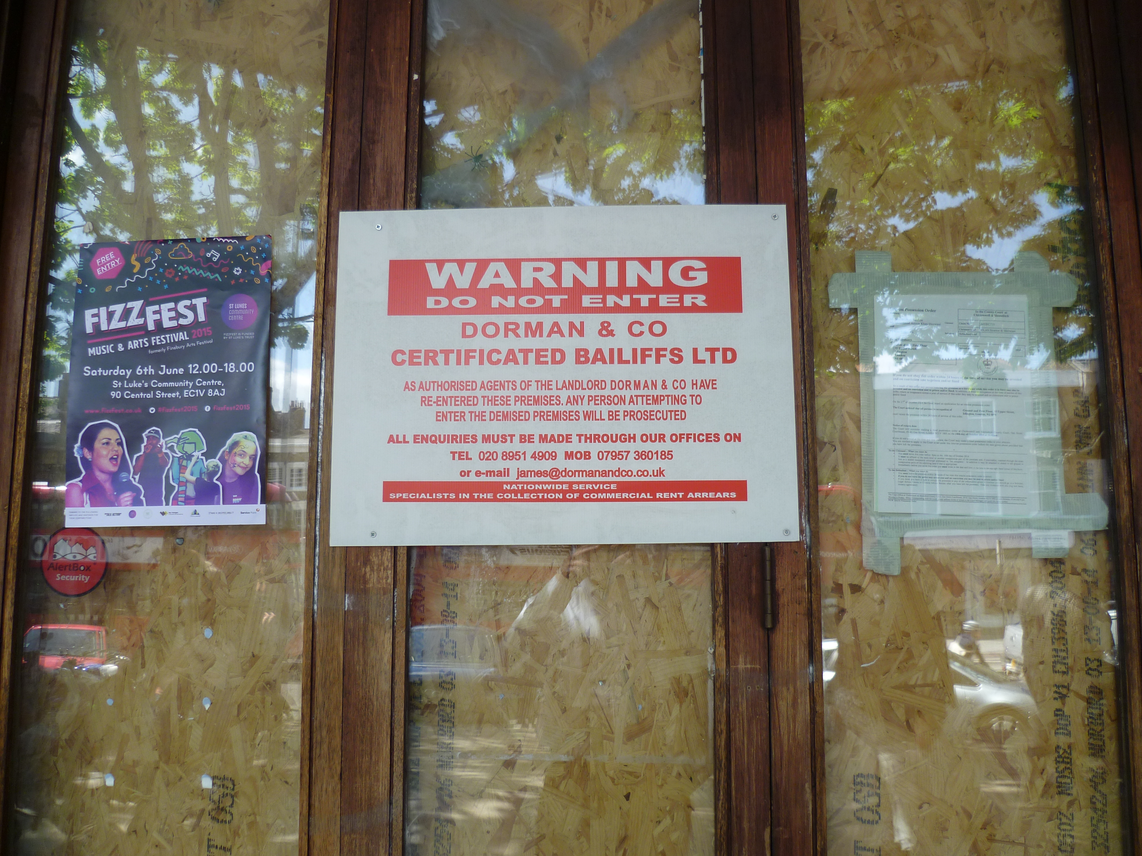 A certificated bailiff's notice on boarded-up premises in London — the visible face of enforcement agents taking control of a debtor's goods under a warrant or writ of control.