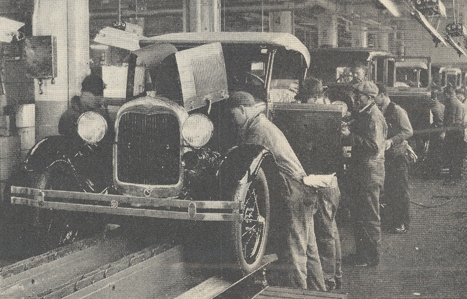 An early Ford Motor Company assembly line demonstrates the division of labor, where workers specialized in specific, repetitive tasks to drastically increase economic efficiency and productivity.