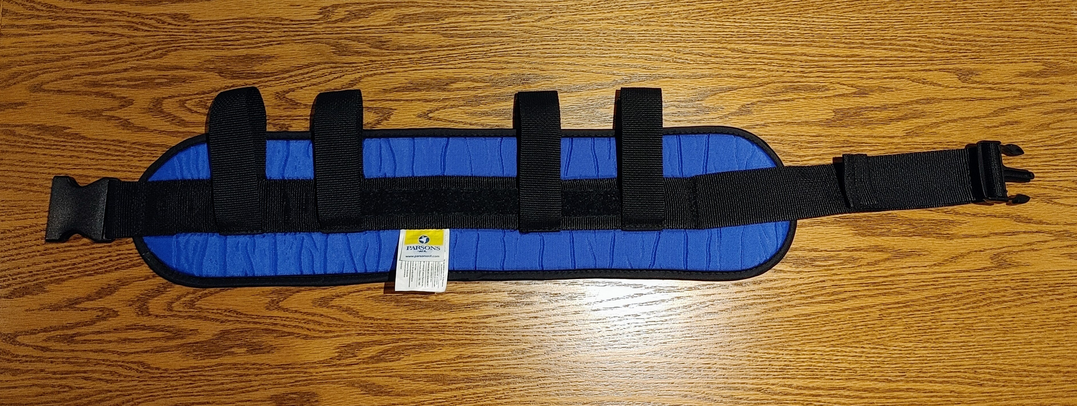A gait belt provides a secure mechanical grip at the client's center of gravity and must be applied over clothing to prevent sheer forces from tearing the skin.