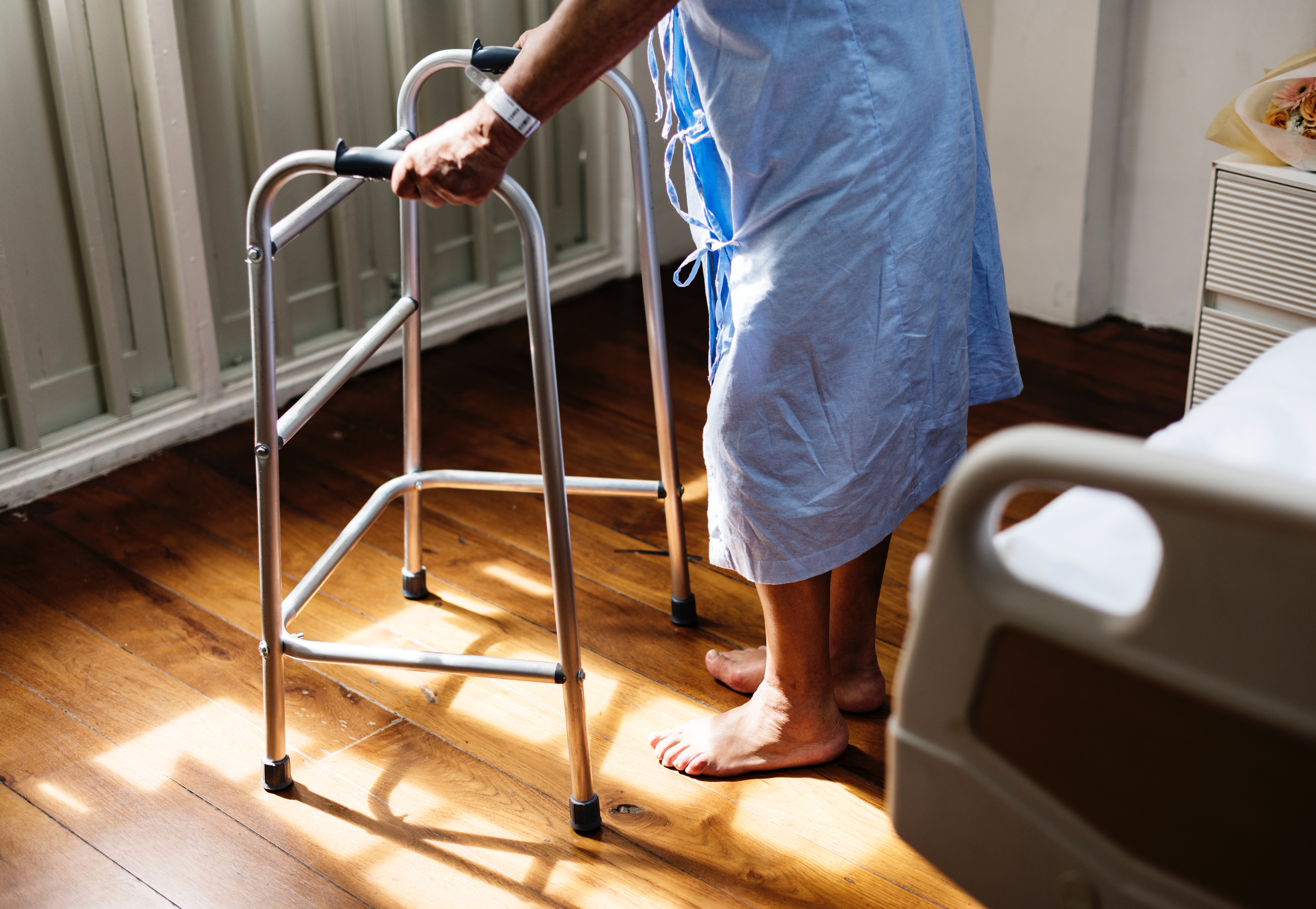 A patient supporting her body weight using a standard non-wheeled walker, demonstrating the required base of stability during the gait sequence.