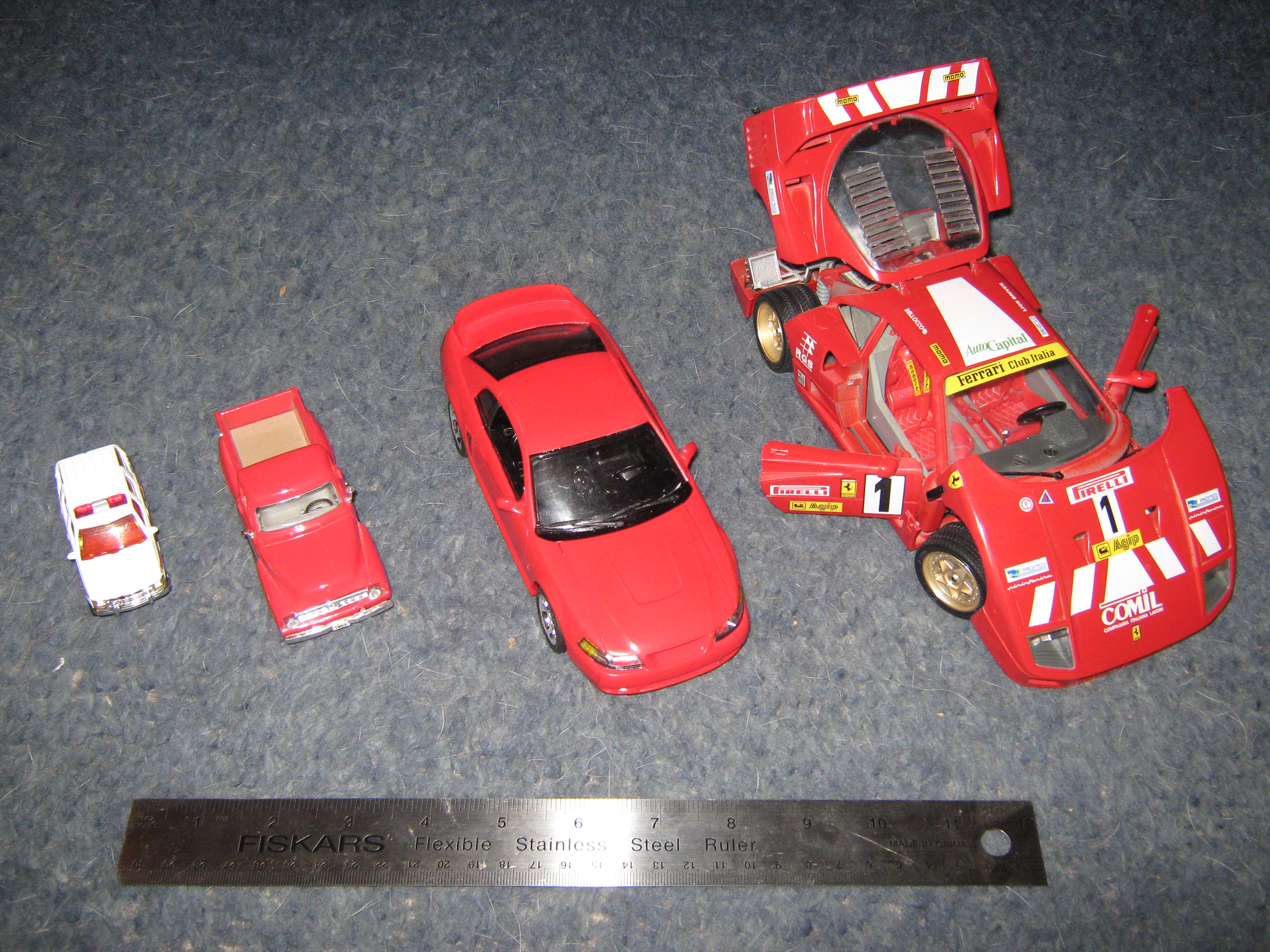 A visual comparison of scale models to an actual measuring ruler, demonstrating how various scale factors (ranging from 1:64 down to 1:18) proportionally reduce the size of the objects.