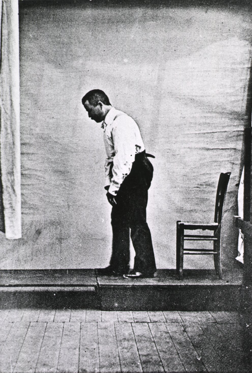A historical medical illustration showing the characteristic forward-leaning posture of a Parkinsonian gait, which dangerously shifts the patient's center of gravity forward and drastically increases the risk of tripping on uneven thresholds.