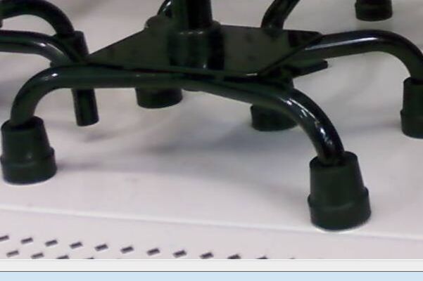 The base of a quad cane. The device must be positioned with its flatter side closest to the patient's body to prevent tripping over the flared legs during the gait cycle.