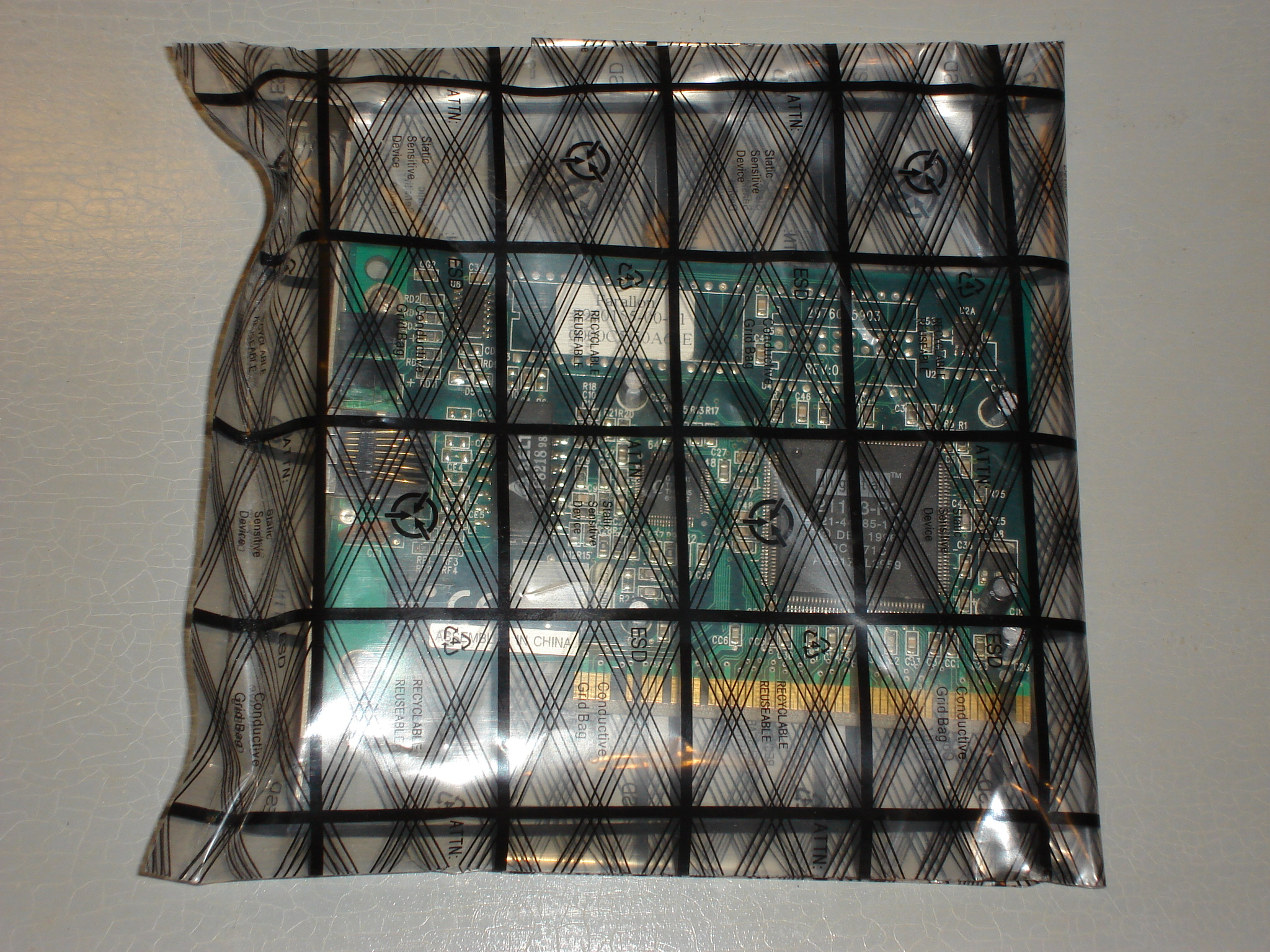 A computer circuit card stored securely inside an anti-static bag, which acts as a localized Faraday cage to shield the delicate electronics from external electrical fields and electrostatic discharge.
