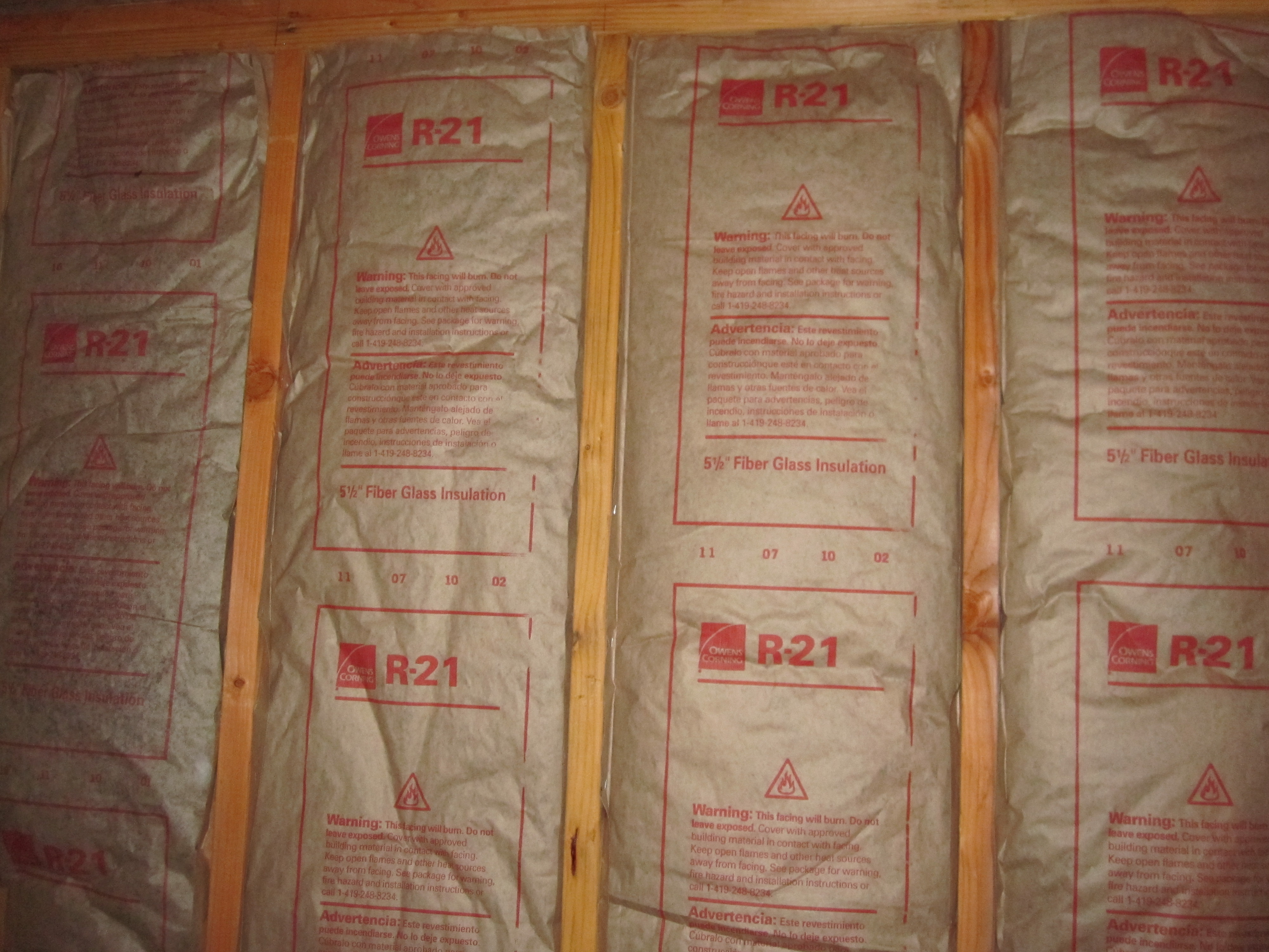 Faced fiberglass batt insulation installed between framing studs. The printed 'R-21' denotes its R-value, explicitly indicating its thermal resistance capability.
