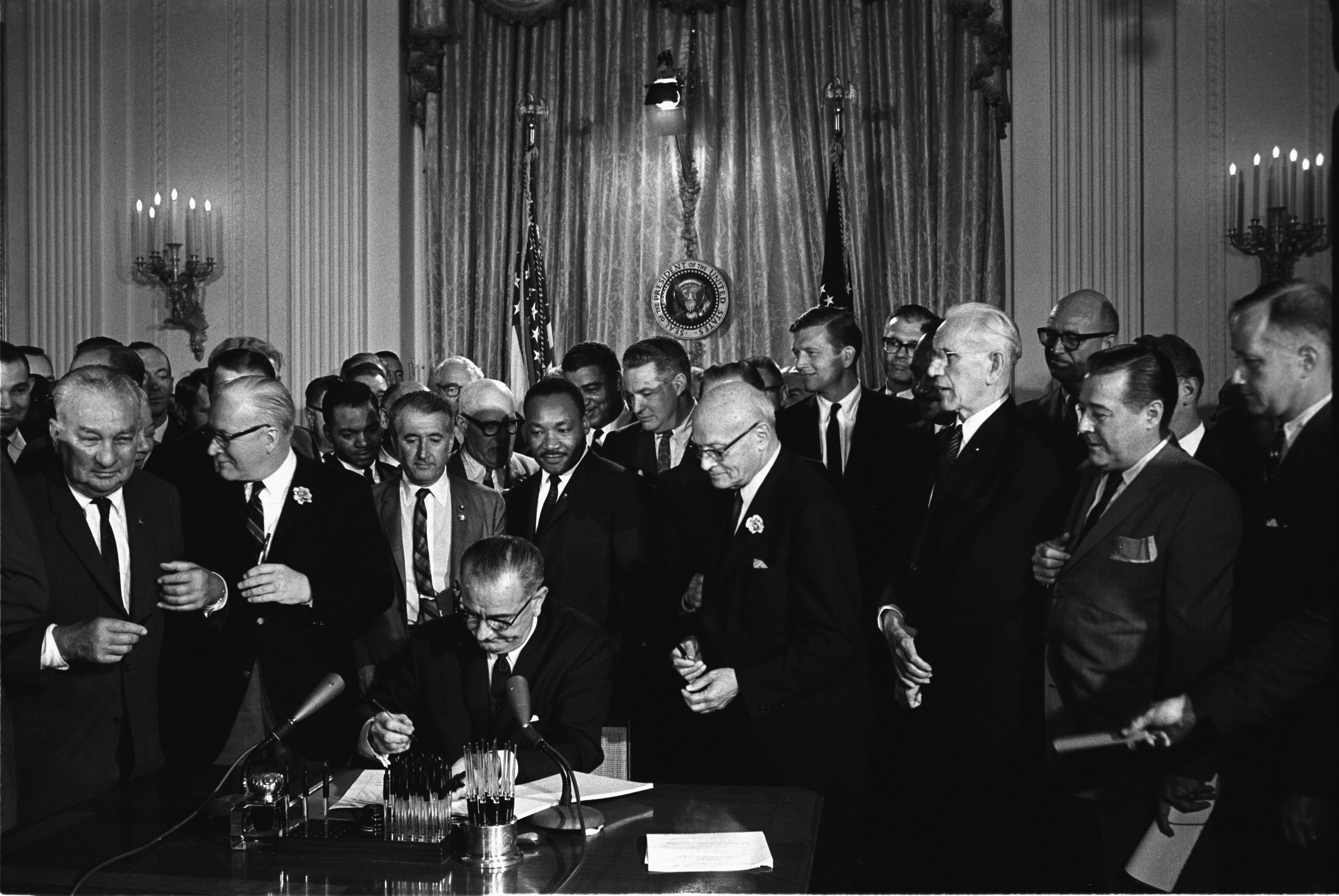 President Lyndon B. Johnson signs the federal Civil Rights Act of 1964. Michigan service provision agreements must include non-discrimination clauses compliant with both federal law and the state's Elliott-Larsen Civil Rights Act.