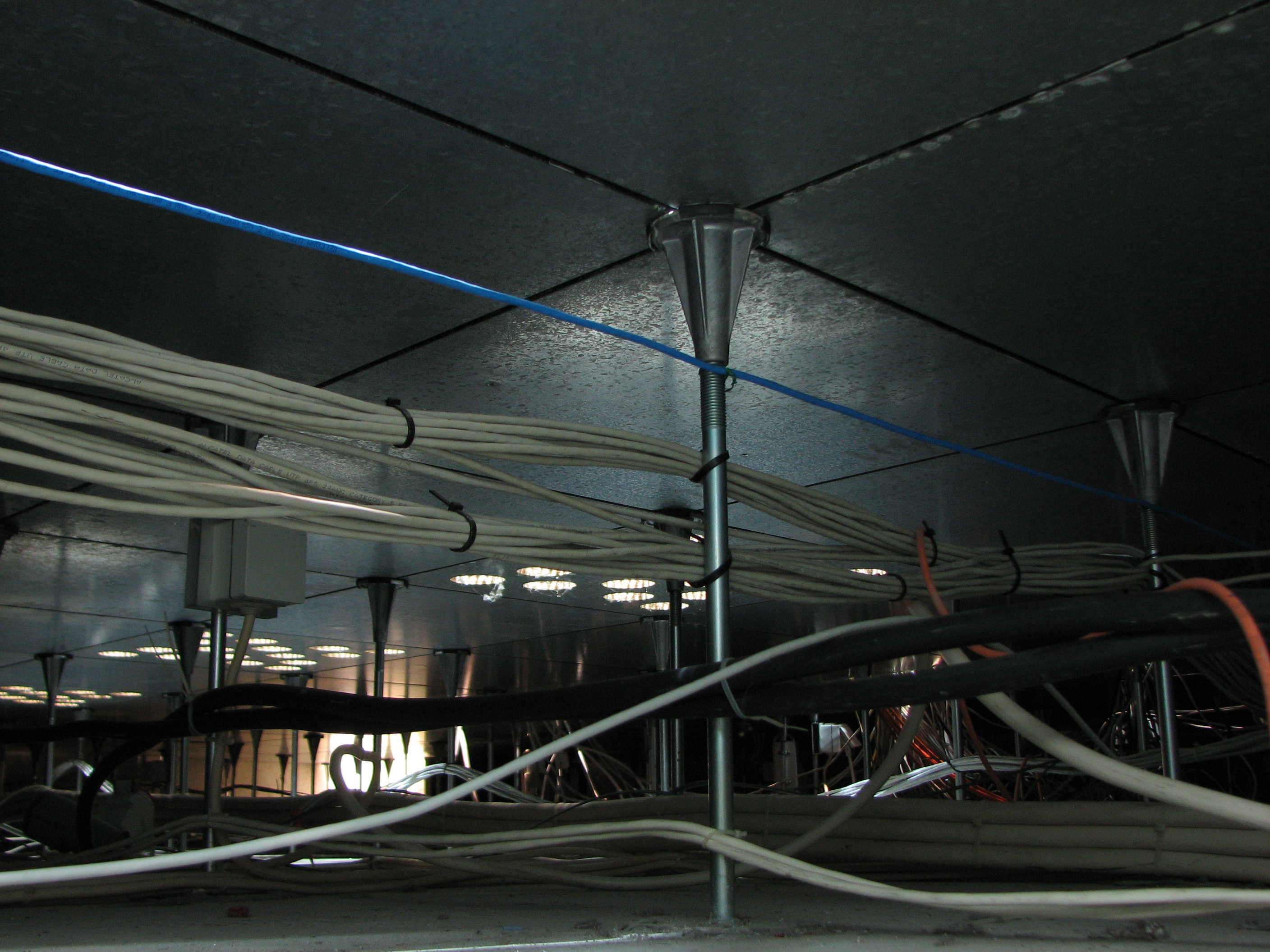 The area beneath a raised floor in a data center, where moisture sensors are typically deployed to immediately detect water leaks near critical cabling and power supplies.